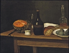Two bottles, an empty wine glass, a knife, a slice of pumpkin, a half loaf of bread, a white napkin with figs and black grapes in a white porcelain bowl, all on a wooden table