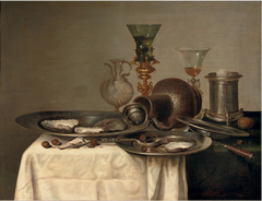 Still life with oysters, fallen jug, wine glasses, hazelnuts, perfume bottle and pewter dishes on a partly draped table by Cornelis Mahu